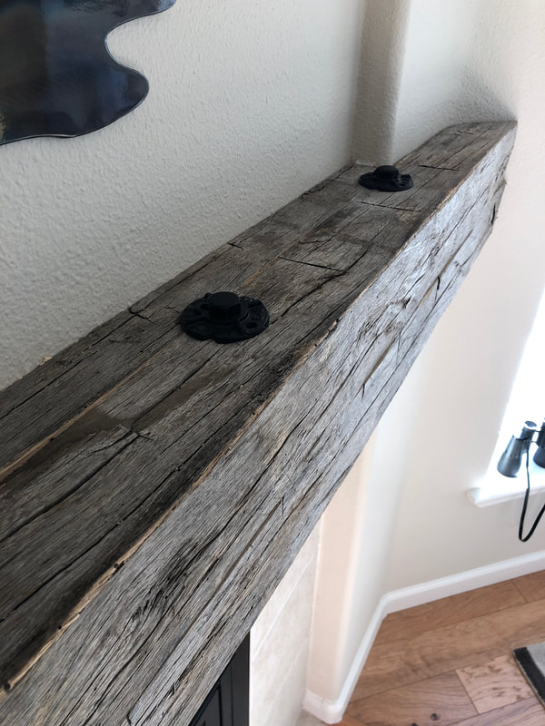 Uo close view of the gray reclaimed hand hewn white oak mantle and industrial bolts.